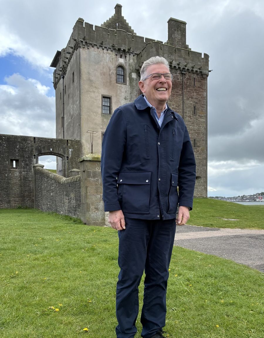 Raymond Edwards, smiling on the grass in front of the castle tower